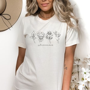 May include: A white t-shirt with a black line drawing of five flowers and the word "elnazima" printed on the front.