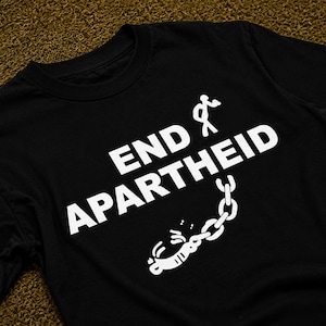 Puede incluir: Una camiseta negra de manga corta con el texto END APARTHEID impreso en blanco. El dise&ntilde;o incluye un gr&aacute;fico de una figura de palo alej&aacute;ndose de una cadena y un grillete rotos, situado sobre las letras blancas en negrita del estampado.
