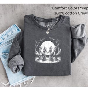May include: A charcoal gray crewneck sweatshirt in the color Pepper, made of 100% cotton. The front features a white graphic illustration of four figures in witch hats holding hands under a full moon, with the text Girls Will Be Girls.