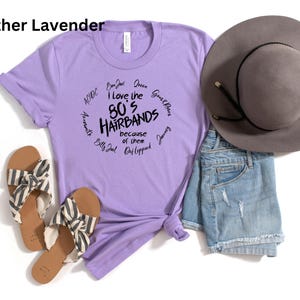 Peut inclure: Un t-shirt lavande avec le texte "I love the 80's Hairbands because of them" et des noms de groupes. Le t-shirt est associ&eacute; &agrave; un short en jean, un chapeau gris et des sandales &agrave; rayures.