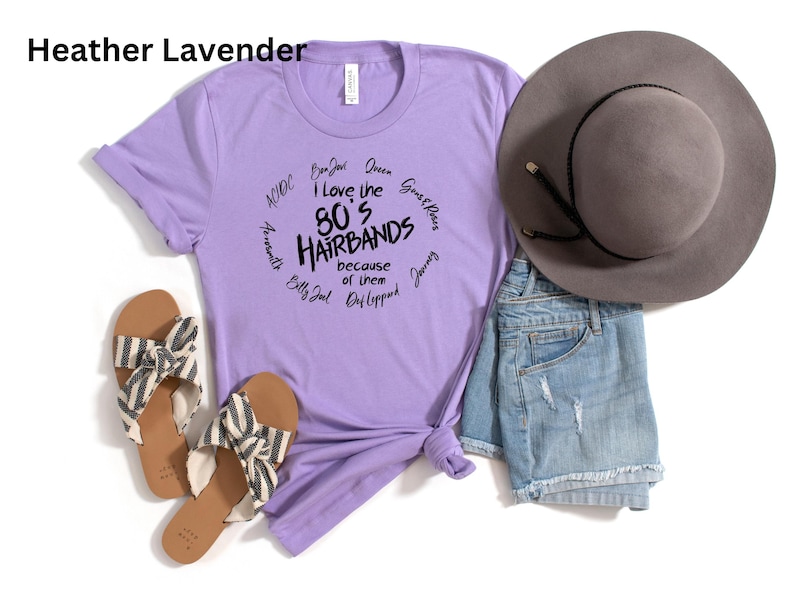 Peut inclure: Un t-shirt lavande avec le texte "I love the 80's Hairbands because of them" et des noms de groupes. Le t-shirt est associ&eacute; &agrave; un short en jean, un chapeau gris et des sandales &agrave; rayures.