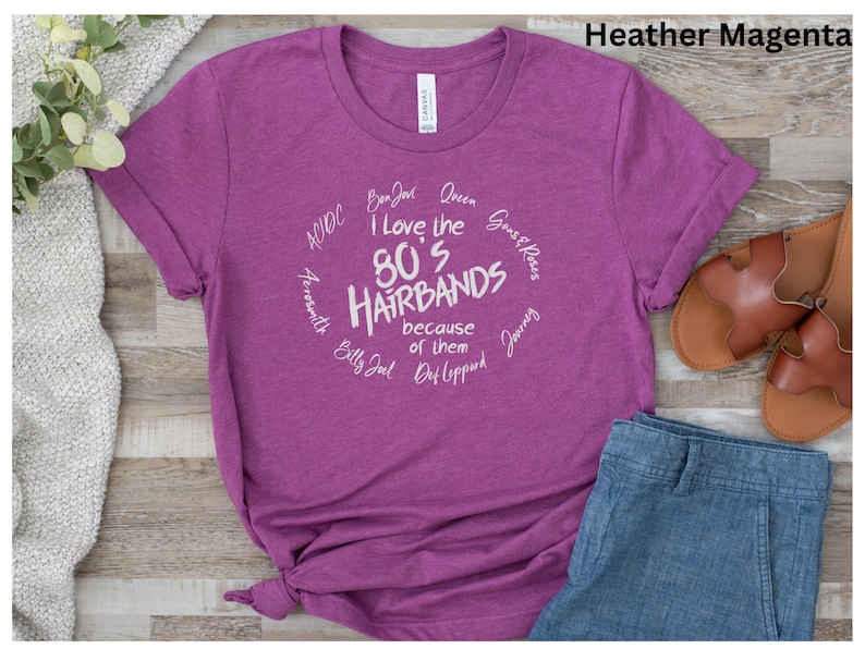 Peut inclure: T-shirt magenta avec l'inscription "I Love the 80's Hairbands" dans un motif circulaire blanc. Le t-shirt comprend des noms de groupes comme Bon Jovi et Def Leppard. Le t-shirt est associ&eacute; &agrave; un jean bleu et des sandales marron.