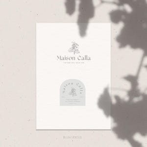 Op de afbeelding: Een witte kaart met een logo voor Maison Calla Interior Design. Het logo toont een gestileerde tekening van een Calla-lelie met de tekst "Maison Calla" en "Interior Design" onder de bloem. De kaart toont ook een kleiner logo met de tekst "Maison Calla" in een cirkel met een gestileerde Calla-lelie in het midden.