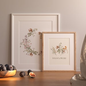 Puede incluir: Dos impresiones bot&aacute;nicas enmarcadas con ilustraciones de flores silvestres. La impresi&oacute;n m&aacute;s grande presenta una corona de flores silvestres, mientras que la impresi&oacute;n m&aacute;s peque&ntilde;a muestra un grupo de flores silvestres con el texto "Flores silvestres" debajo.