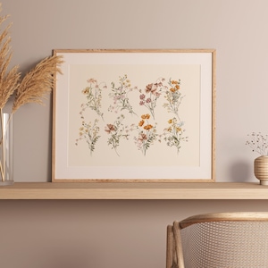 Puede incluir: Una impresi&oacute;n enmarcada de una ilustraci&oacute;n bot&aacute;nica que presenta una colecci&oacute;n de delicadas flores silvestres en tonos de rosa, naranja y amarillo. La impresi&oacute;n se muestra en un estante de madera con un jarr&oacute;n de hierba de la pampa seca y un peque&ntilde;o jarr&oacute;n de flores secas.