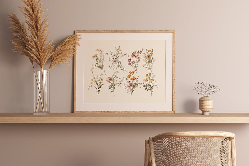 Puede incluir: Una impresi&oacute;n enmarcada de una ilustraci&oacute;n bot&aacute;nica que presenta una colecci&oacute;n de delicadas flores silvestres en tonos de rosa, naranja y amarillo. La impresi&oacute;n se muestra en un estante de madera con un jarr&oacute;n de hierba de la pampa seca y un peque&ntilde;o jarr&oacute;n de flores secas.
