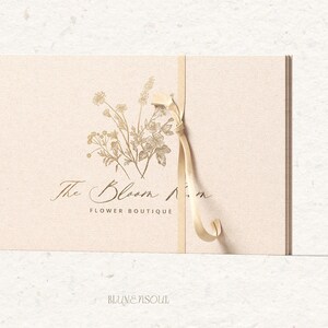 May include: A beige card with a gold ribbon tied around it. The card has a floral design and the text "The Bloom Room Flower Boutique".