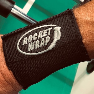 May include: Black wrist wrap with white embroidered text that reads "ROCKET WRAP".
