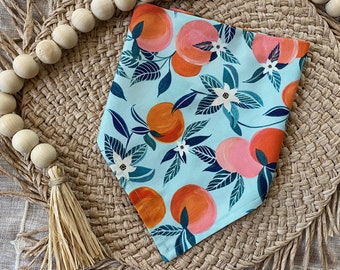 May include: A light blue bandana with a pattern of pink and orange oranges, green leaves, and white flowers. The bandana is on a woven straw mat.