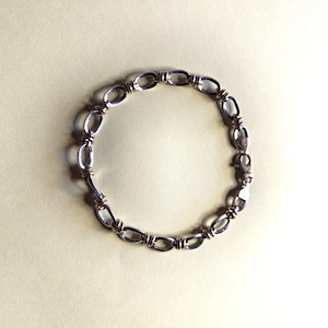 May include: A silver-toned metal chain bracelet featuring a series of oval-shaped links connected by smaller, triple-wrapped wire segments. The bracelet includes a secure lobster claw clasp mechanism for fastening, showcasing a polished finish.