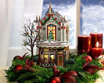 May include: A miniature Christmas village house with a green roof and white trim. The house has a sign that reads "Christmas Treasures". The house is surrounded by a green wreath with red and gold ornaments.