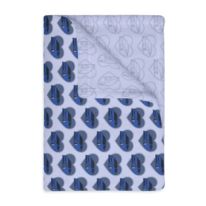Könnte beinhalten: Eine hellblaue Decke mit einem sich wiederholenden Muster aus blauen, gesichtsähnlichen Figuren in grauen Herzen. Die Rückseite hat ein ähnliches Design in einem helleren Grau. Die Decke ist gefaltet und zeigt beide Seiten des Designs.