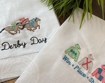 May include: Two embroidered tea towels. One features a line of horses with jockeys and the text "Derby Day". The other features three jockey silks with the text "Win, Place, Show".