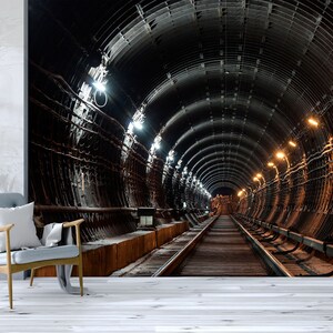 May include: A dark, industrial tunnel with a long, straight track running down the centre. The tunnel is lined with metal beams and pipes, and there are several lights illuminating the space. The tunnel appears to be very long and extends far into the distance.