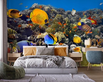 Könnte beinhalten: Ein Schlafzimmer mit einem Wandbild, das eine lebendige Unterwasserszene mit bunten Fischen zeigt, die zwischen Korallenriffen schwimmen. Das Wandbild zeigt eine Vielzahl von Fischen, darunter gelbe, blaue und orangefarbene Fische. Das Schlafzimmer hat auch ein Bett mit einem weißen Bettbezug und einem blauen Kissen.