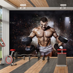Puede incluir: Un hombre musculoso levantando pesas en un gimnasio. El hombre está sin camisa y lleva pantalones cortos grises. El fondo es oscuro y humeante con un foco que ilumina al hombre.