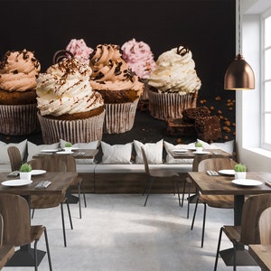 Pode incluir: Uma mesa com duas mesas e cadeiras de madeira, com um mural de parede de cupcakes com cobertura de chocolate e baunilha. Os cupcakes são decorados com granulado de chocolate e um redemoinho de chocolate.