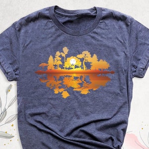 May include: A navy blue t-shirt with a graphic of a sunset reflected in a lake with trees on the shore.