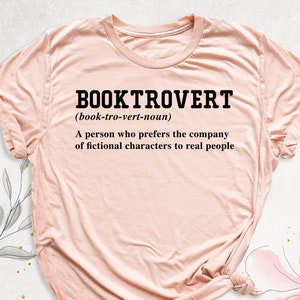 May include: A pink t-shirt with the text "BOOKTROVERT (book-tro-vert-noun) A person who prefers the company of fictional characters to real people" printed in black.