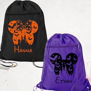May include: Two drawstring backpacks, one black and one purple. The black bag features an orange Halloween design with a bow, bats, and a castle, with the name "Hanna". The purple bag has a black design with bats and a castle, with the name "Ethan".