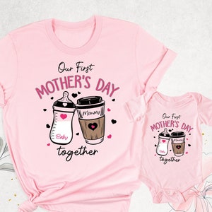 May include: Pink t-shirt and onesie set with a graphic of a baby bottle and a coffee cup. The text reads "Our First Mother's Day together".