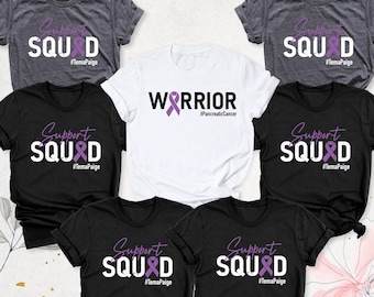 May include: Five t-shirts with different designs. Two are black with white text that says "Support Squad" with a purple ribbon. Two are grey with white text that says "Support Squad" with a purple ribbon. One is white with black text that says "Warrior" with a purple ribbon. All shirts have the hashtag "#TemaPaige" printed on them.