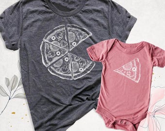 May include: A dark heather gray short-sleeve t-shirt featuring a white line-art graphic of a whole pizza cut into slices, paired with a dusty rose short-sleeve baby bodysuit featuring a single white line-art pizza slice graphic.
