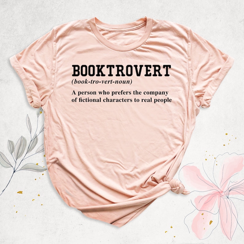 May include: A pink t-shirt with the text "BOOKTROVERT (book-tro-vert-noun) A person who prefers the company of fictional characters to real people" printed in black.