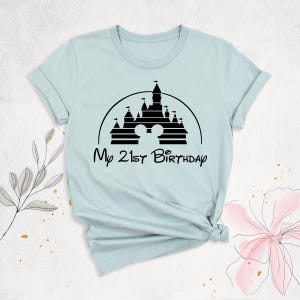 May include: Light blue t-shirt with a black silhouette of the Disney castle and the text "My 21st Birthday".