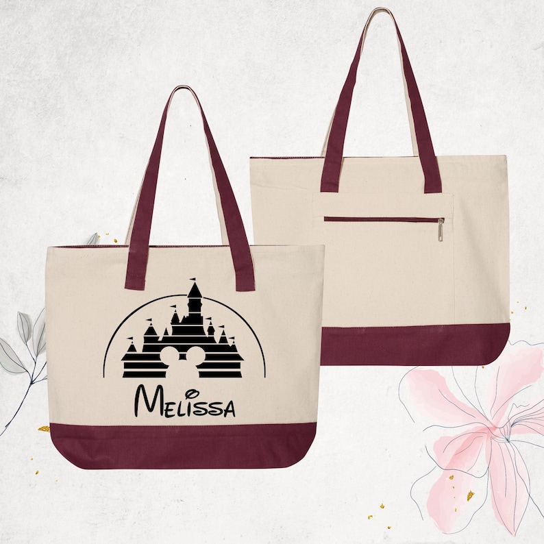 Pu&ograve; includere: Una borsa tote in tela bianca con manici e bordo inferiore marroni. La borsa presenta una silhouette nera del castello Disney con le orecchie di Topolino al centro e il nome "Melissa" stampato sotto.