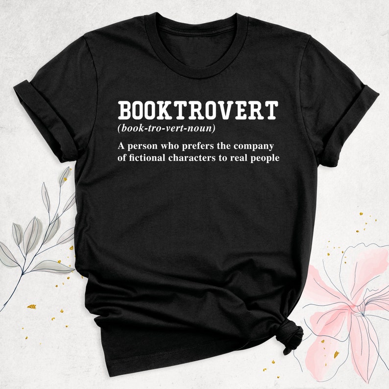 May include: Black t-shirt with white text that reads "BOOKTROVERT (book-tro-vert-noun) A person who prefers the company of fictional characters to real people."
