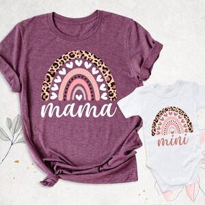 Puede incluir: Un conjunto de dos camisetas con un arco&iacute;ris con detalles de estampado de leopardo y corazones. La camiseta m&aacute;s grande dice "mama" y la m&aacute;s peque&ntilde;a dice "mini".