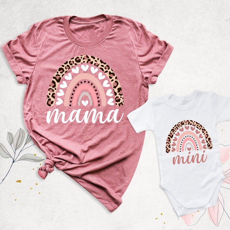 Puede incluir: Una camiseta rosa y blanca con un dise&ntilde;o de arco&iacute;ris y la palabra "mama" impresa en ella. Un body blanco con un dise&ntilde;o de arco&iacute;ris y la palabra "mini" impresa en &eacute;l.