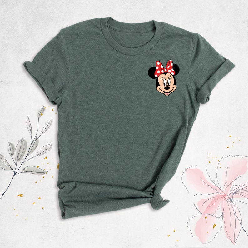 Puede incluir: Una camiseta verde con una imagen de dibujos animados de Minnie Mouse con un lazo rojo con lunares blancos.