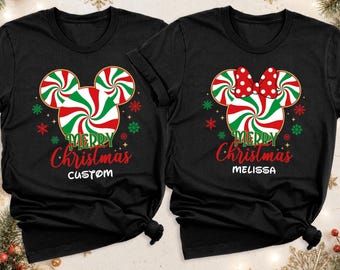 May include: Two black t-shirts featuring a red, white, and green peppermint candy graphic shaped like mouse ears. The left shirt says Merry Christmas CUSTOM, and the right shirt says Merry Christmas MELISSA, with a red and white polka dot bow.