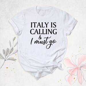 May include: White t-shirt with black text that reads "ITALY IS CALLING & I must go".