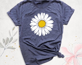 May include: A heather navy blue short-sleeve t-shirt featuring a large, centered graphic of a white daisy flower with a bright yellow center. The shirt has a crew neckline and a casual fit, showcasing a simple floral design on the front.