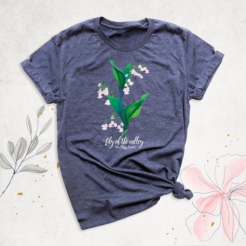 May include: A dark heather grey t-shirt with a white graphic of a lily of the valley flower. The text "Lily of the valley, the May flower" is printed below the flower.