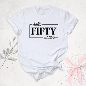 K&ouml;nnte beinhalten: Wei&szlig;es T-Shirt mit schwarzem Text, der "hello FIFTY est. 1973" lautet.