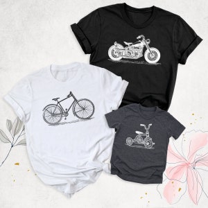 May include: Three t-shirts featuring different vintage vehicle designs. A white t-shirt with a bicycle, a black t-shirt with a motorcycle, and a grey t-shirt with a tricycle.