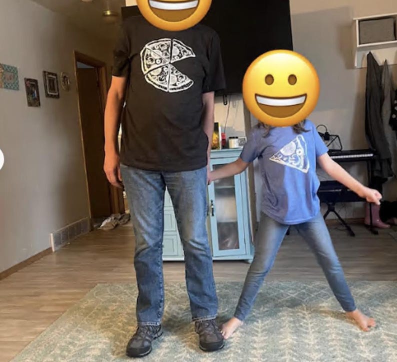 以下が含まれることがあります： 一切れ欠けたピザの白いグラフィックが描かれた黒い半袖Tシャツと青いデニムジーンズ、グレーのスニーカー、そしてピザ一切れの白いグラフィックが描かれた水色の半袖Tシャツ。