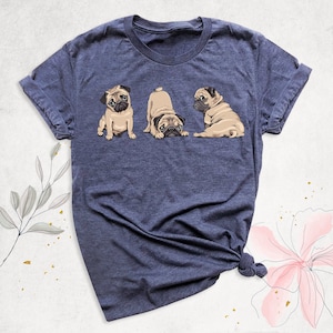 May include: A navy blue t-shirt with a graphic of three pugs. The pugs are in different poses, one is sitting, one is looking back, and one is looking forward.