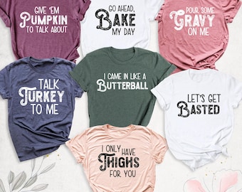 May include: A collection of seven short-sleeved crew neck t-shirts in various colors including maroon, white, pink, navy, dark green, and light pink. Each shirt features black or white text with phrases like Give 'em Pumpkin to Talk About, Go Ahead Bake My Day, Pour Some Gravy on Me, Talk Turkey to Me, I Came in Like a Butterball, Let's Get Basted, and I Only Have Thighs for You.