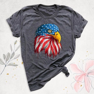 May include: Dark gray t-shirt featuring a graphic of an American bald eagle's head. The eagle's head is designed with the American flag, with blue stars on the head and red and white stripes on the chest. The eagle has a yellow beak.