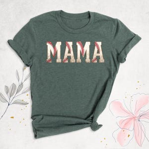 May include: A green t-shirt with the word "MAMA" printed on it in white letters. The letters are outlined with a red baseball stitch design.