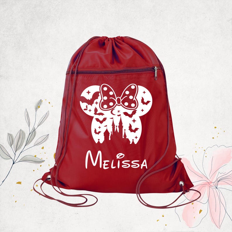 Pu&ograve; includere: Uno zaino a sacca rosso con una grafica bianca raffigurante una silhouette di orecchie di topo con un fiocco a pois, pipistrelli e un castello. Il nome Melissa &egrave; stampato in bianco sotto la grafica. La borsa include una tasca frontale con cerniera.