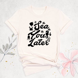 Peut inclure: Un t-shirt blanc avec un motif noir qui dit "Sea You Later" avec des illustrations de la vie marine.