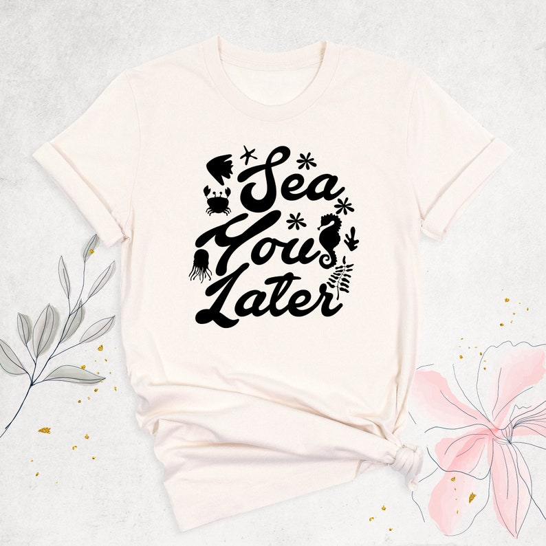 Peut inclure: Un t-shirt blanc avec un motif noir qui dit "Sea You Later" avec des illustrations de la vie marine.