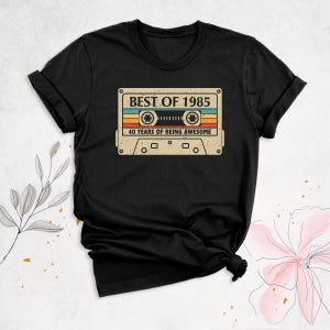 K&ouml;nnte beinhalten: Schwarzes T-Shirt mit einem Vintage-Kassettenband-Motiv, auf dem "Best of 1985, 40 Years of Being Awesome" steht.