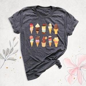 May include: A dark gray t-shirt with a colorful ice cream cone design. The ice cream cones are decorated with sprinkles, cherries, and chocolate.